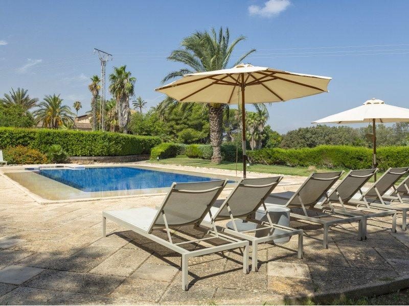 Outdoor swimming pool at Casal Santa Eulalia lined with sun loungers and cream parasols, framed by palm trees and hedges