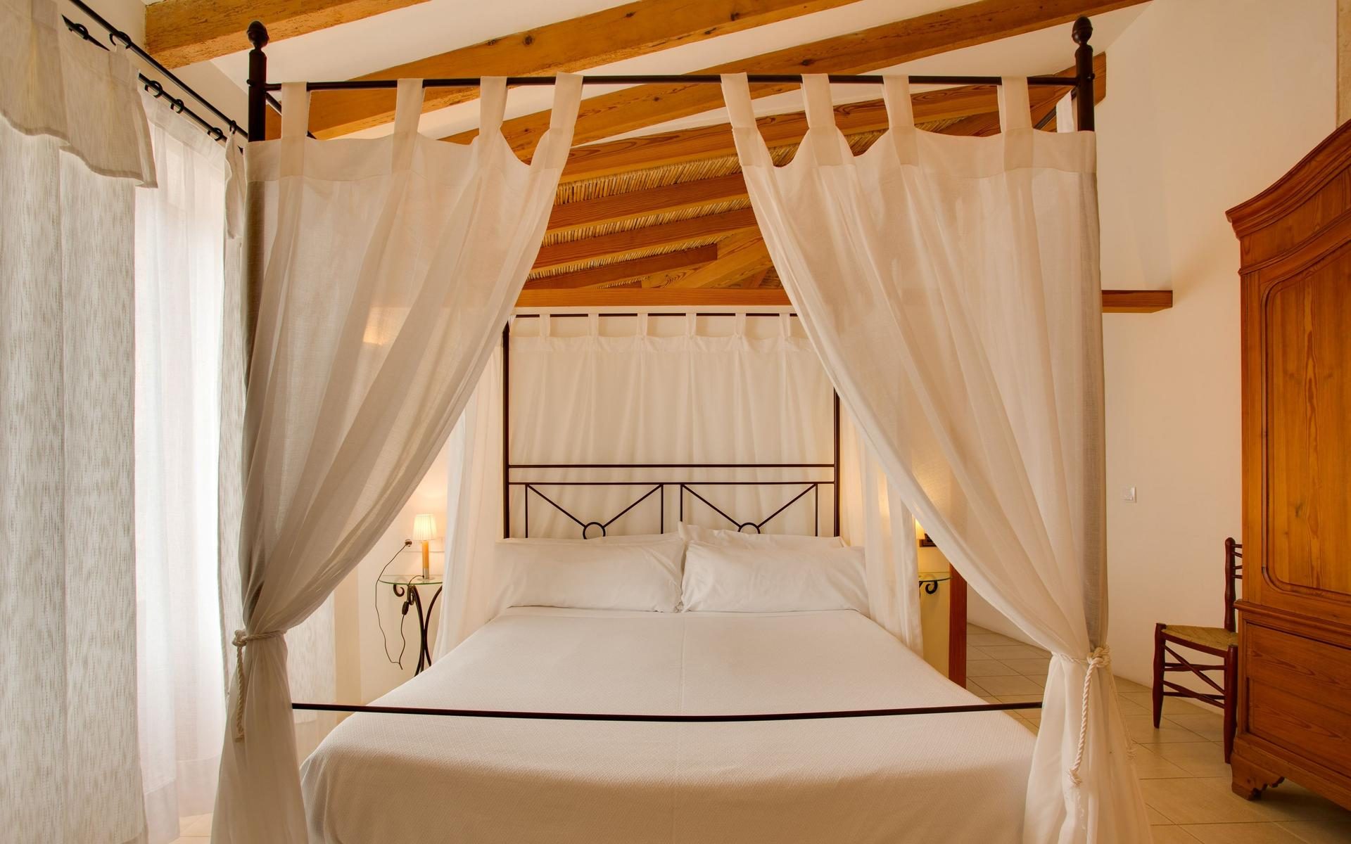 Junior suite at Casal Santa Eulalia with a white canopy bed under an exposed wood-beam ceiling and a antique pine wardrobe