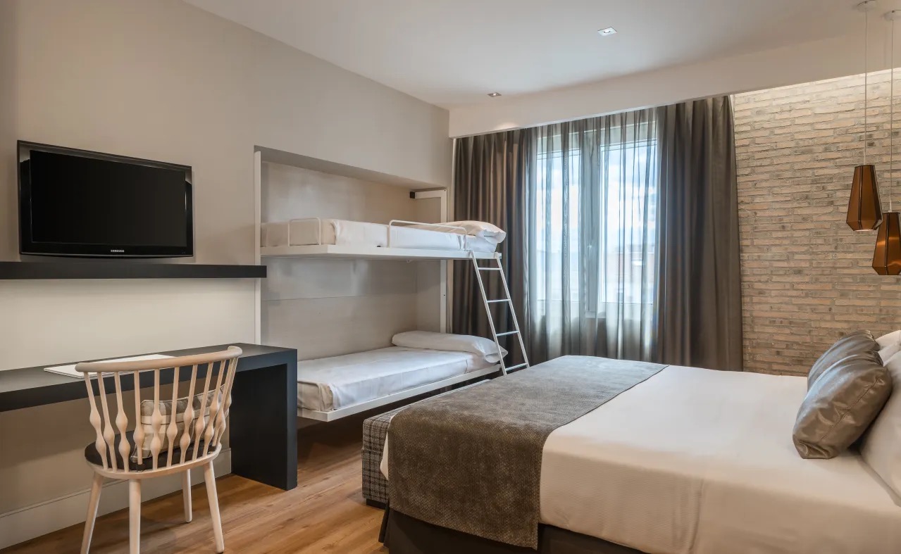 A family room with a fold-down bunk bed next to a standard double bed, a wall-mounted TV and a writing desk.