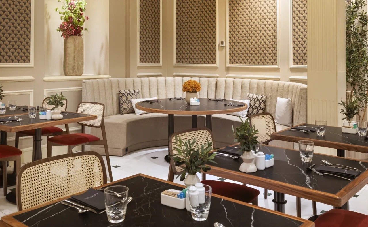 Dining area at Catalonia Las Cortes with black marble-topped tables, cane-backed chairs and a curved cream banquette.