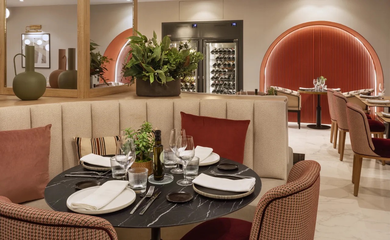 A restaurant dining room with a round marble table set for two, banquette seating, a wine display case and terracotta-coloured arched alcoves.