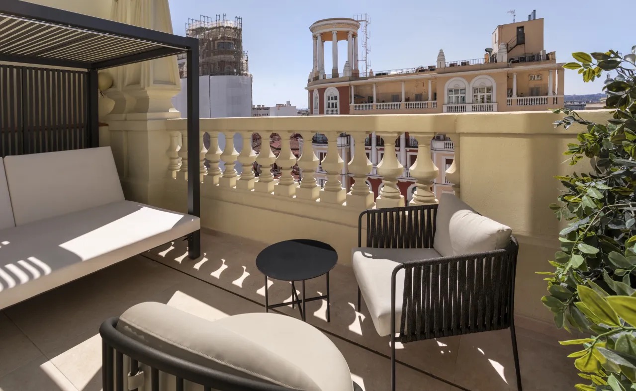 A rooftop terrace with a daybed, lounge chairs and a low table, looking out over Madrid rooftops and a domed corner building.