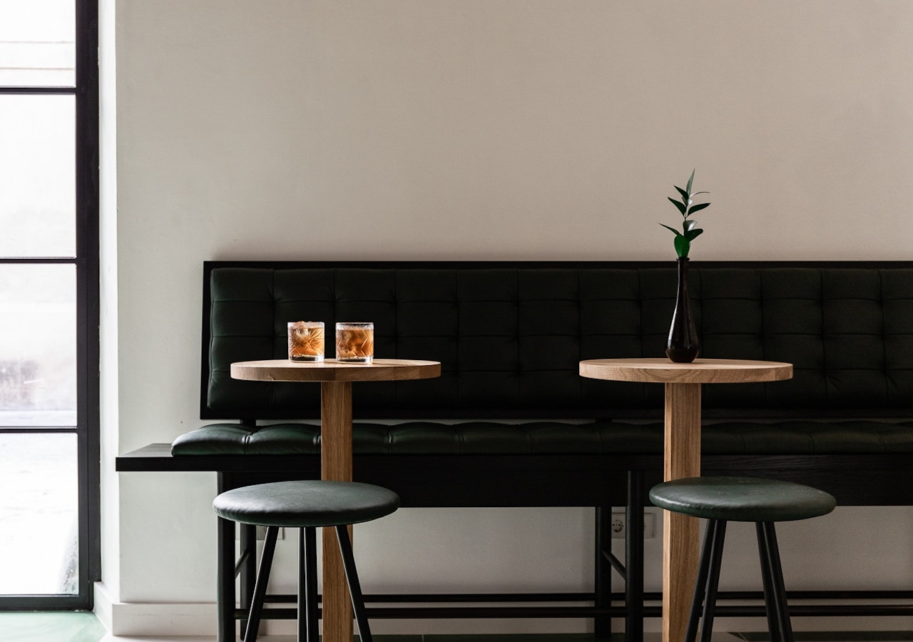High top tables and green stools against a tufted leather banquette in the bar