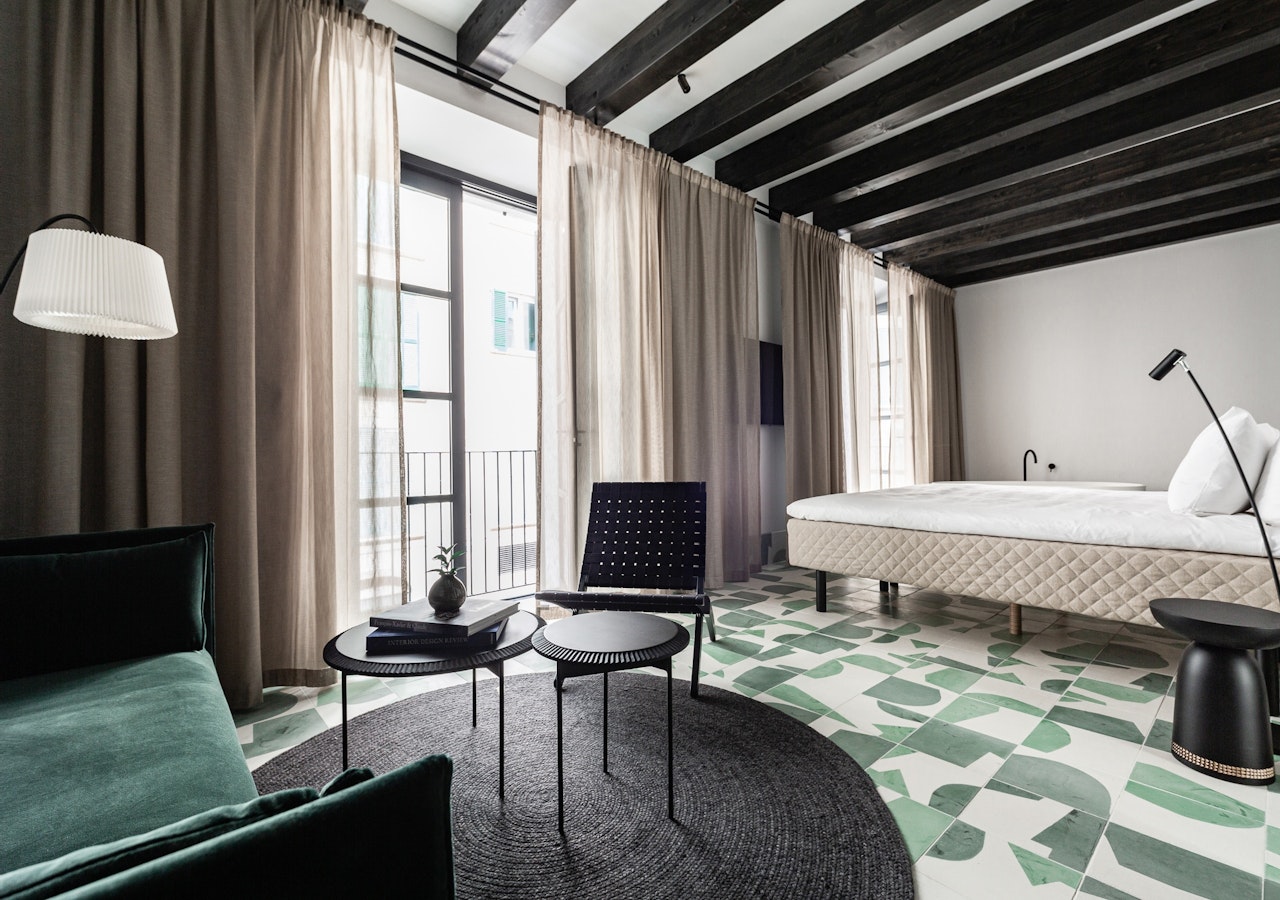 Junior suite with green tiled floor, dark wood ceiling beams and a green velvet sofa
