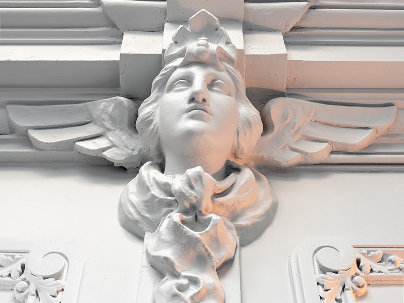 A close-up of a carved white plaster winged figure above the hotel's entrance, the sculpture the hotel's own site describes as the god Hermes.