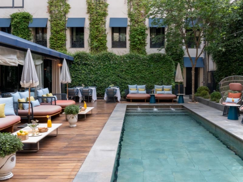 The courtyard pool garden, with wooden decking, orange and blue outdoor sofas, and ivy-covered walls behind the pool.