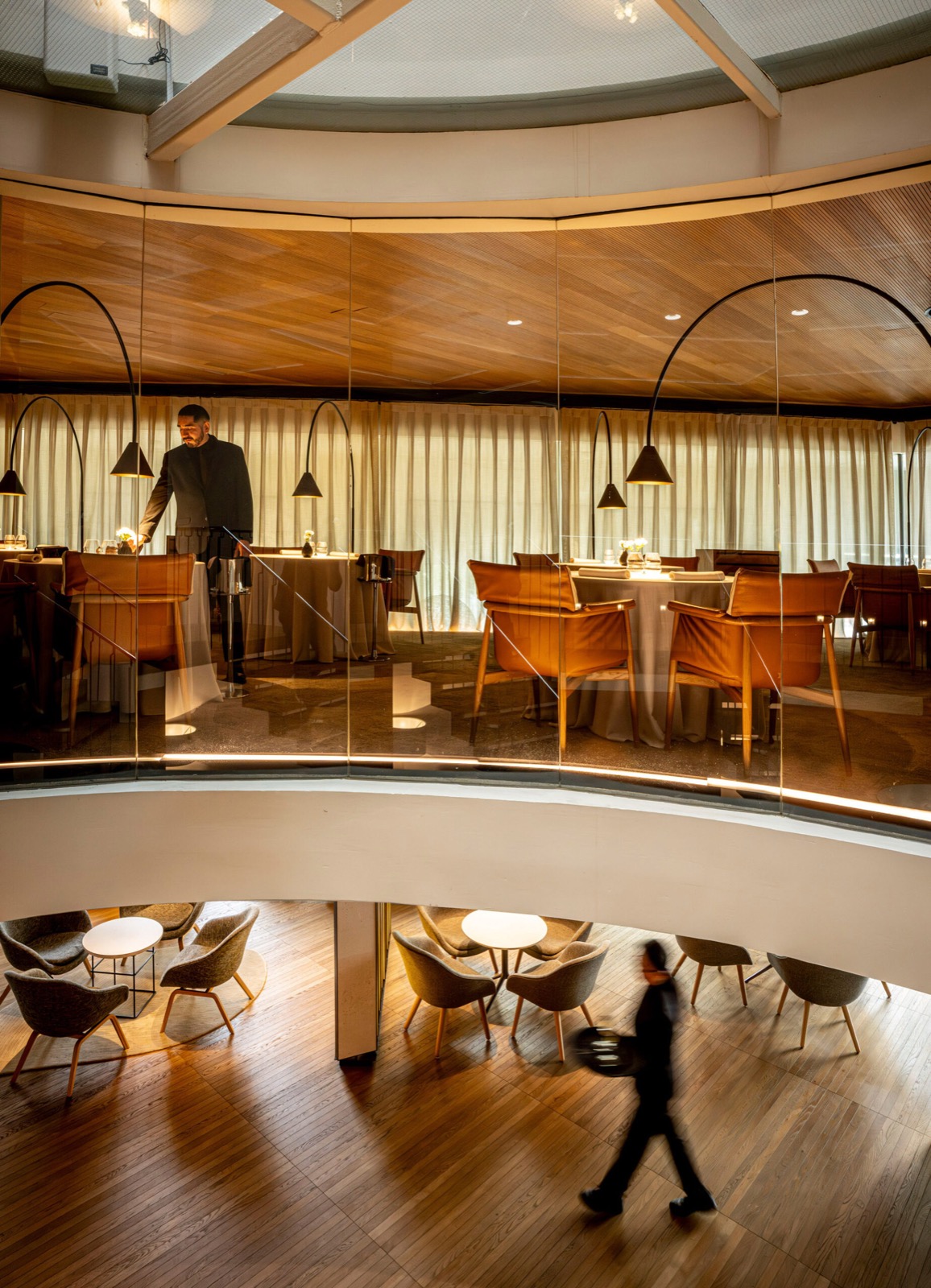 Curved glass-walled dining room of the ABaC restaurant with orange leather chairs