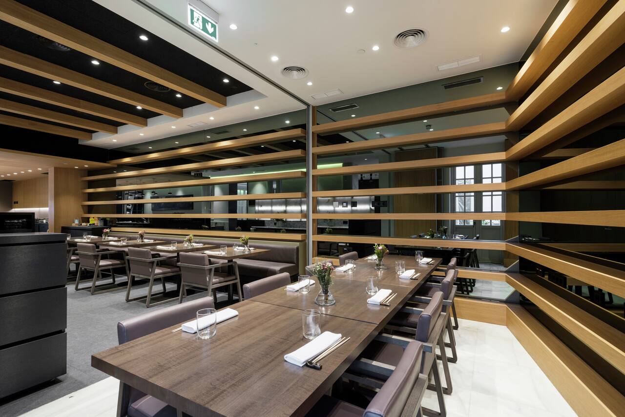 The dining room of Kyoshi, with wood-slat shelving, long tables set with chopsticks and napkins, and an open kitchen counter in the background.