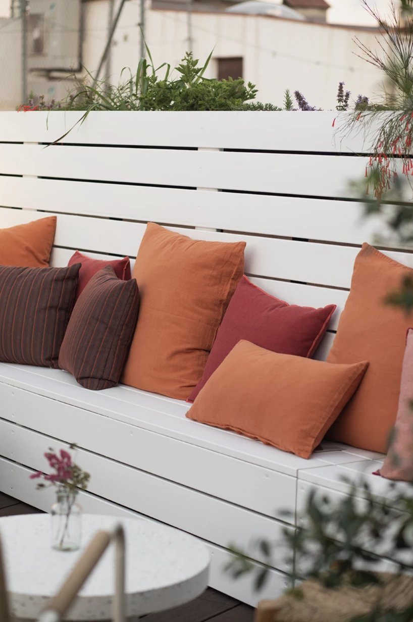 Built-in white bench with orange and red cushions and planters on the rooftop terrace at Eco Boutique Hostal Grau