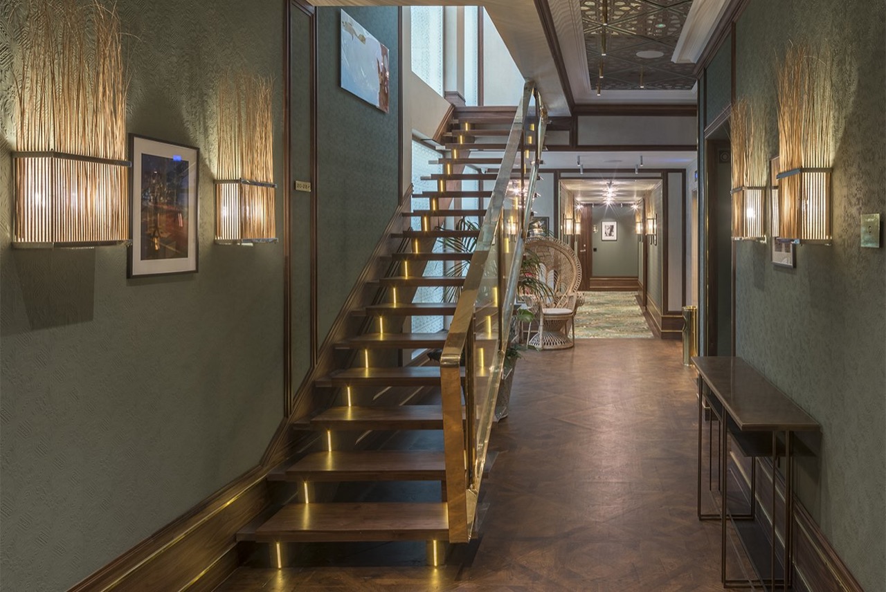 Wood and brass staircase inside El Llorenc, lit by wall sconces along a corridor