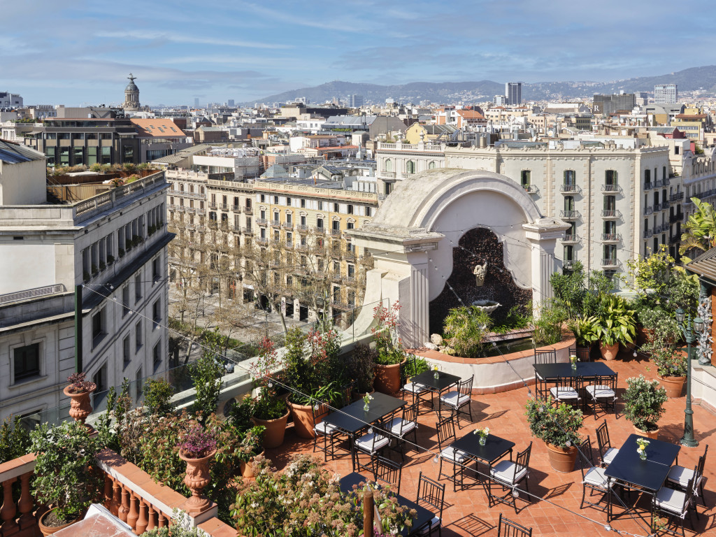Rooftop Garden terrace with dining tables, potted plants and a Barcelona skyline view