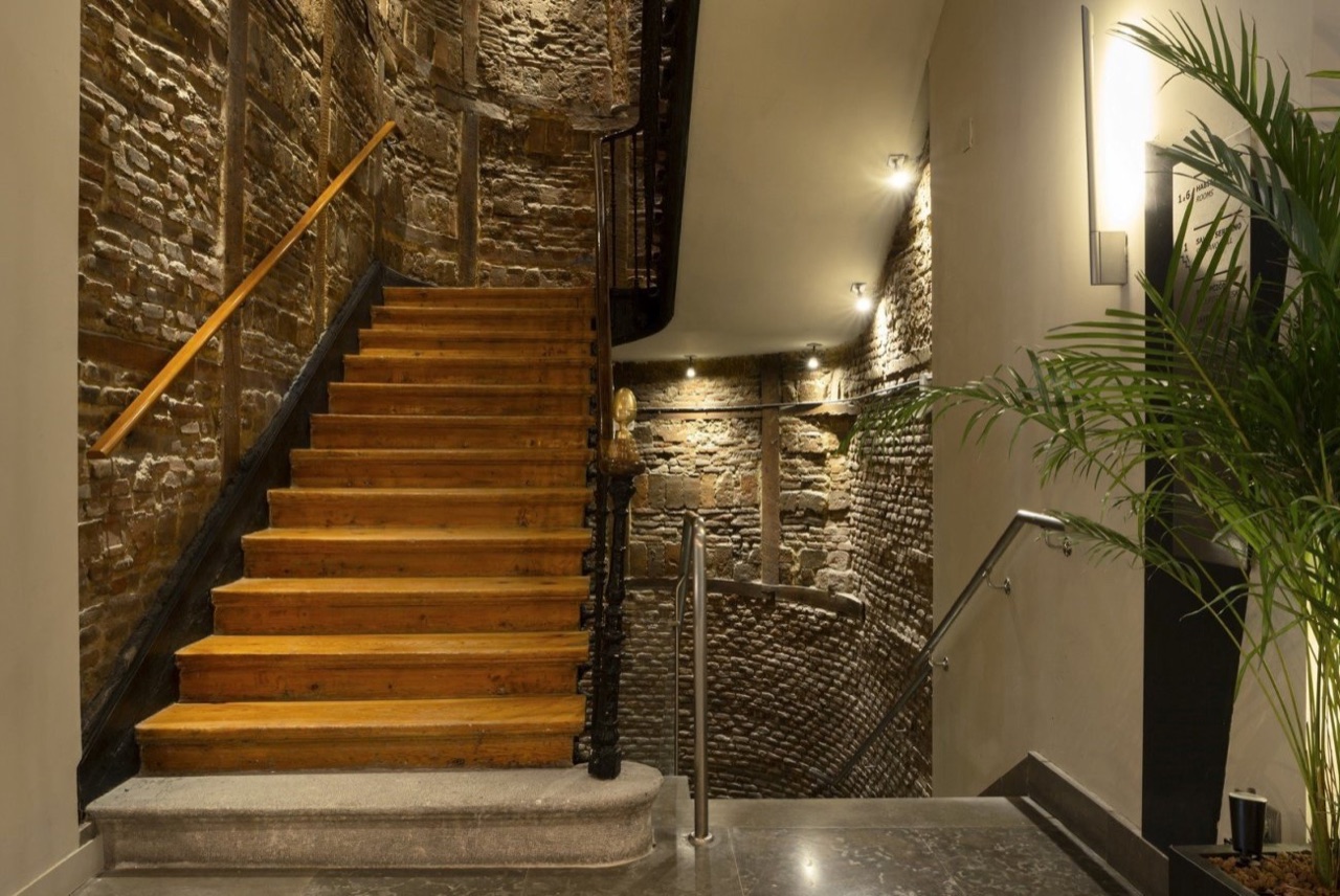 Original wooden staircase with a curved handrail set against exposed old stone and brick walls near the hotel's entrance.