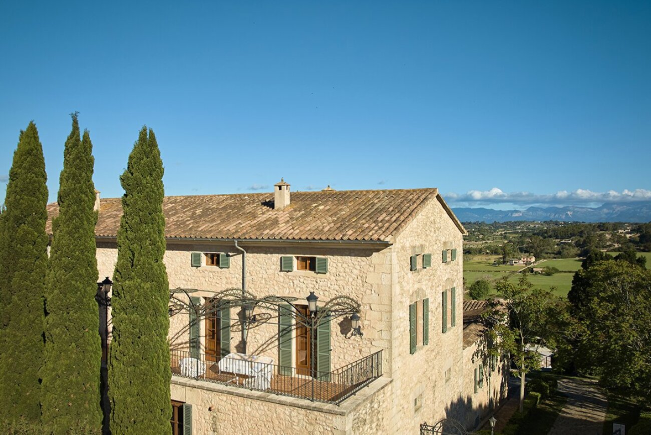 Stone building with green shutters and a balcony behind cypress trees