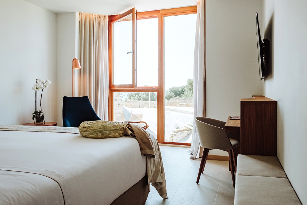Superior room at Es Princep with a wood-framed window open to the terrace and a blue accent chair