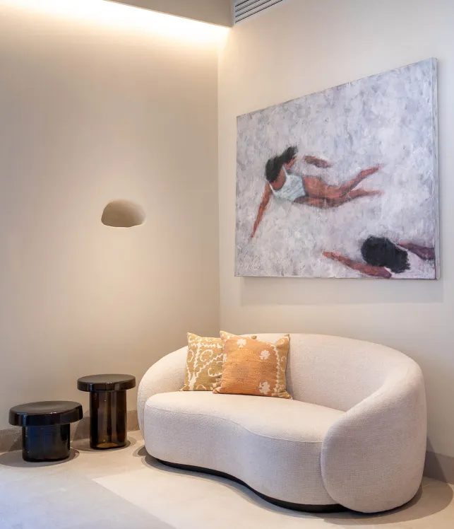 Lounge corner at Finca Banyols with a curved cream boucle sofa, patterned orange cushions and a large beach-scene painting on the wall