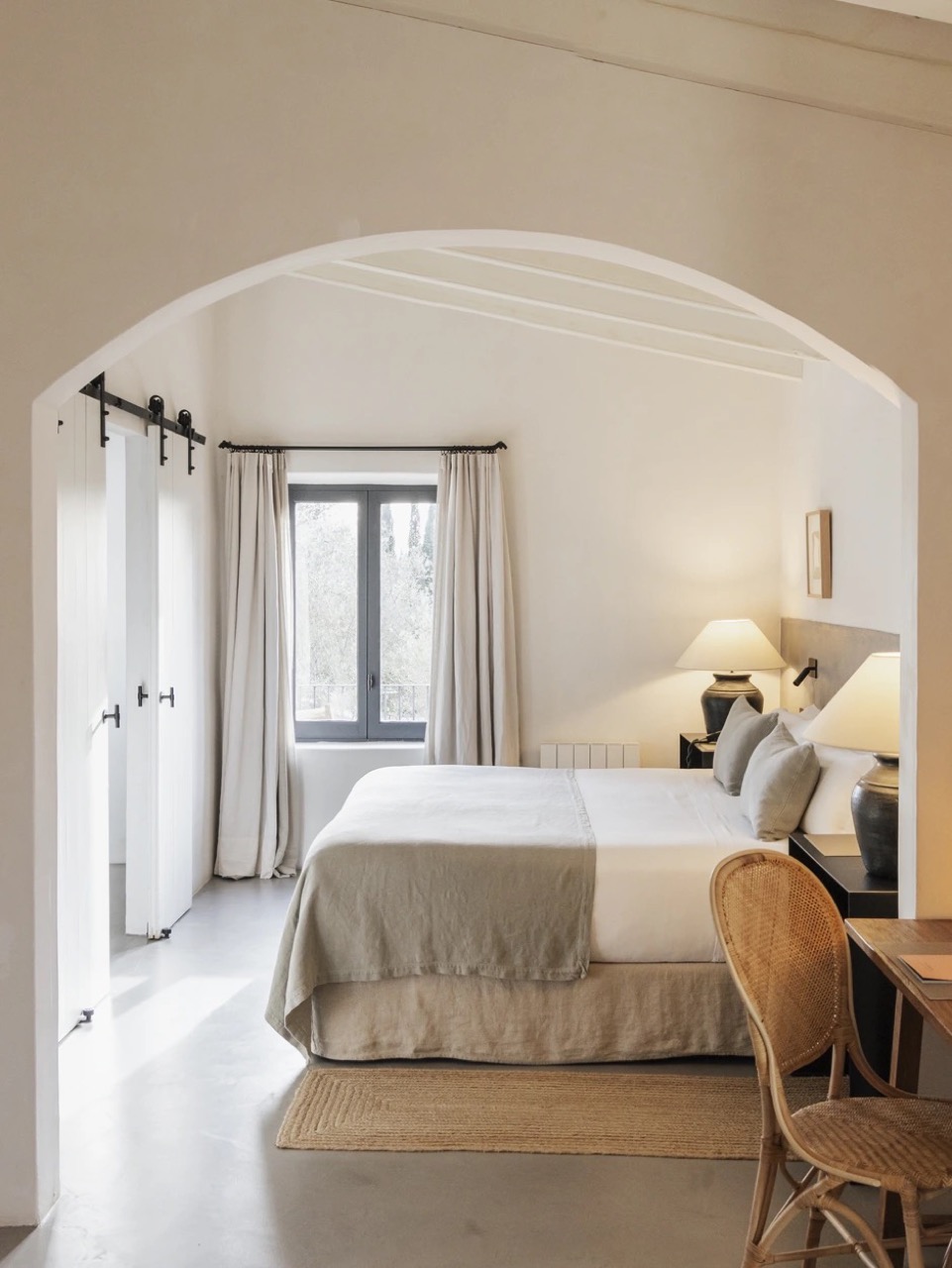 Bedroom at Finca Serena seen through a whitewashed archway, with a bed, desk, and window onto the grounds