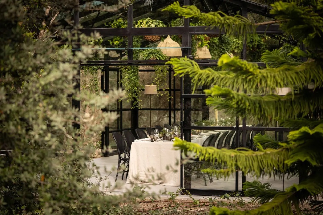 Glass and iron dining pavilion set among trees in the gardens at Finca Serena, with a table laid for dinner