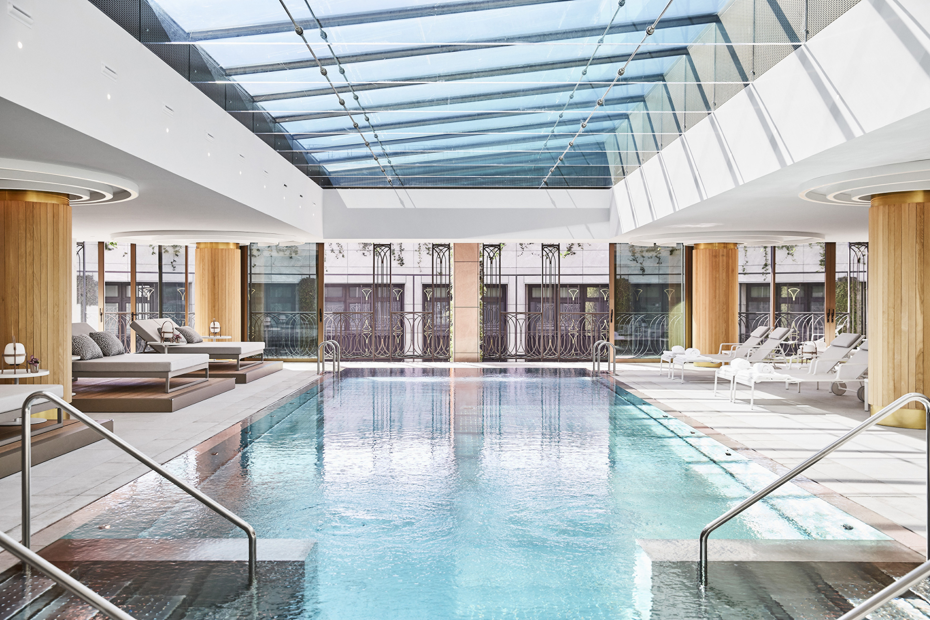 Indoor pool under a slanted glass skylight, lined with cushioned loungers between wooden columns.