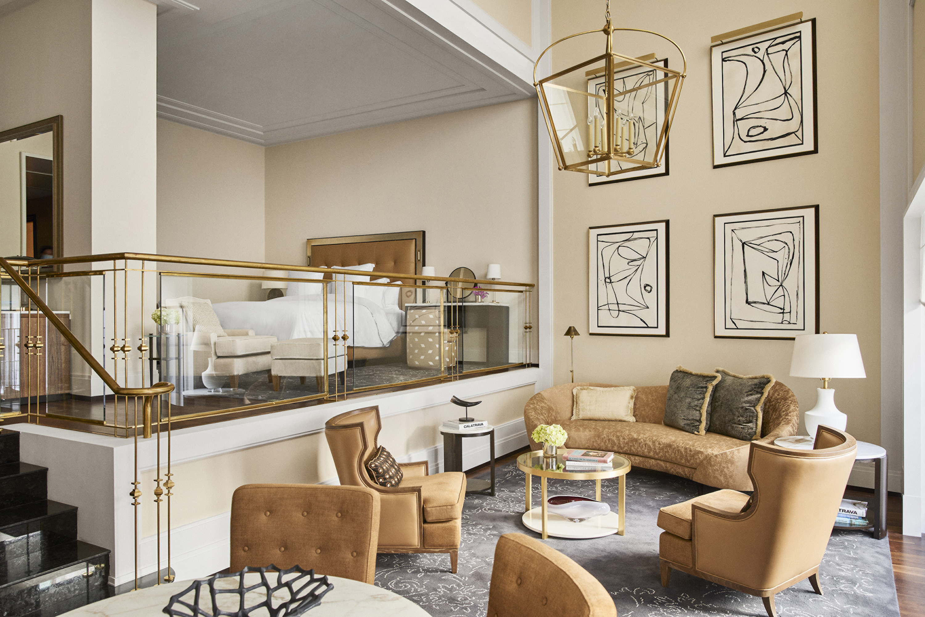 Split-level suite with a curved sofa and armchairs beneath a brass-railed mezzanine bedroom.