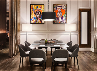 A private dining room with a long table set for eight, grey upholstered chairs, a black pendant lamp and two colourful pop-art paintings on panelled walls.