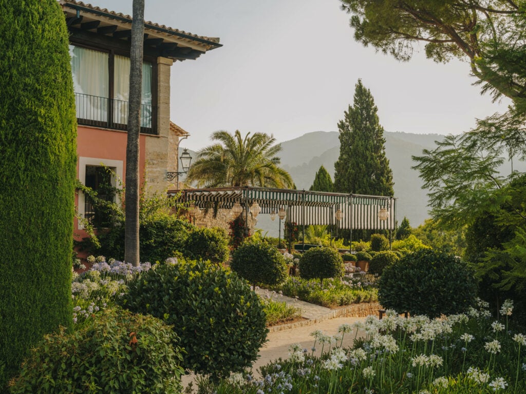 Hotel facade and terrace seen through manicured gardens with mountain backdrop