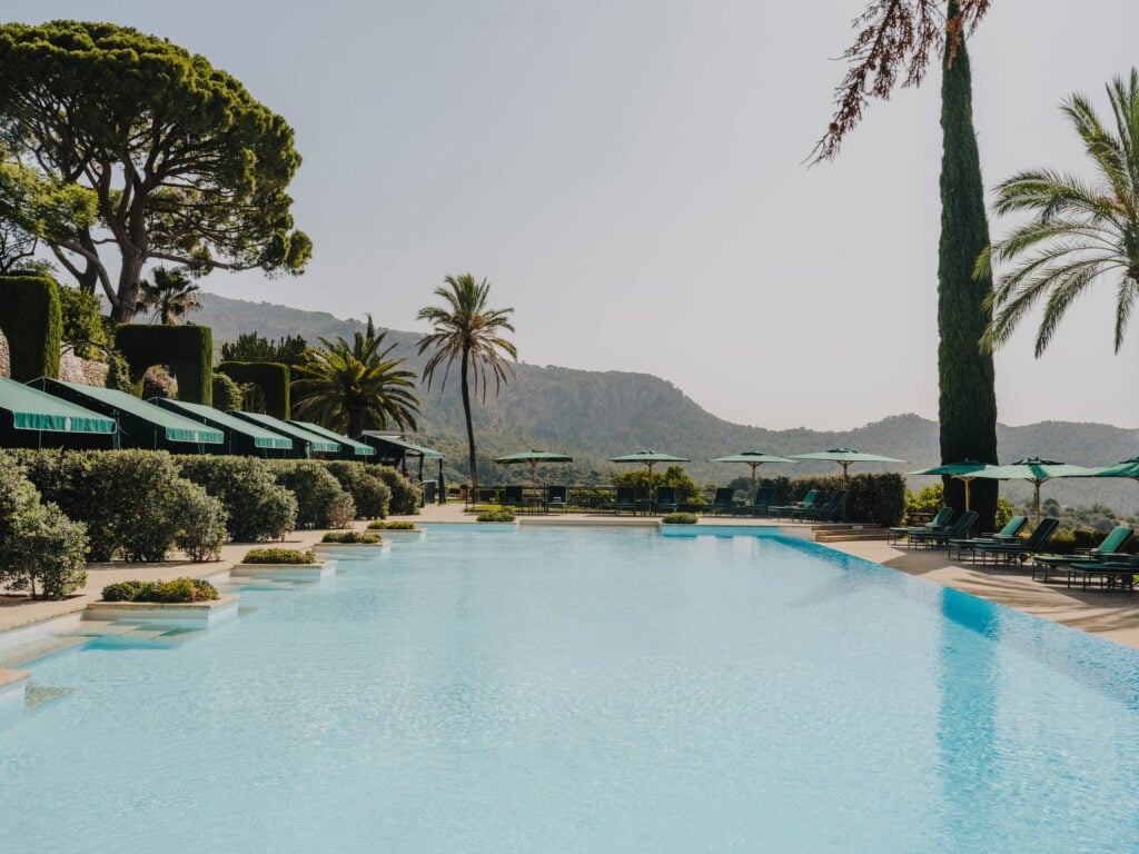 Long pool lined with green umbrellas and loungers facing the Tramuntana mountains