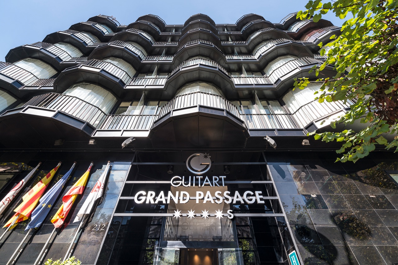 Low angle view of the Guitart Grand Passage facade, showing its tiered scalloped glass balconies and ground floor signage at Carrer de Muntaner 212.