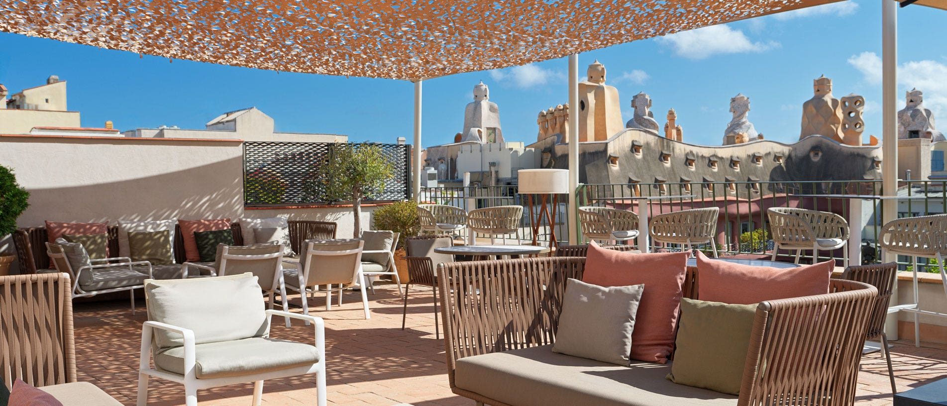 El Cel de Gaudi rooftop terrace at H10 Casa Mimosa with wicker lounge seating under a shade canopy, facing the chimneys of Gaudi's Casa Mila across the street
