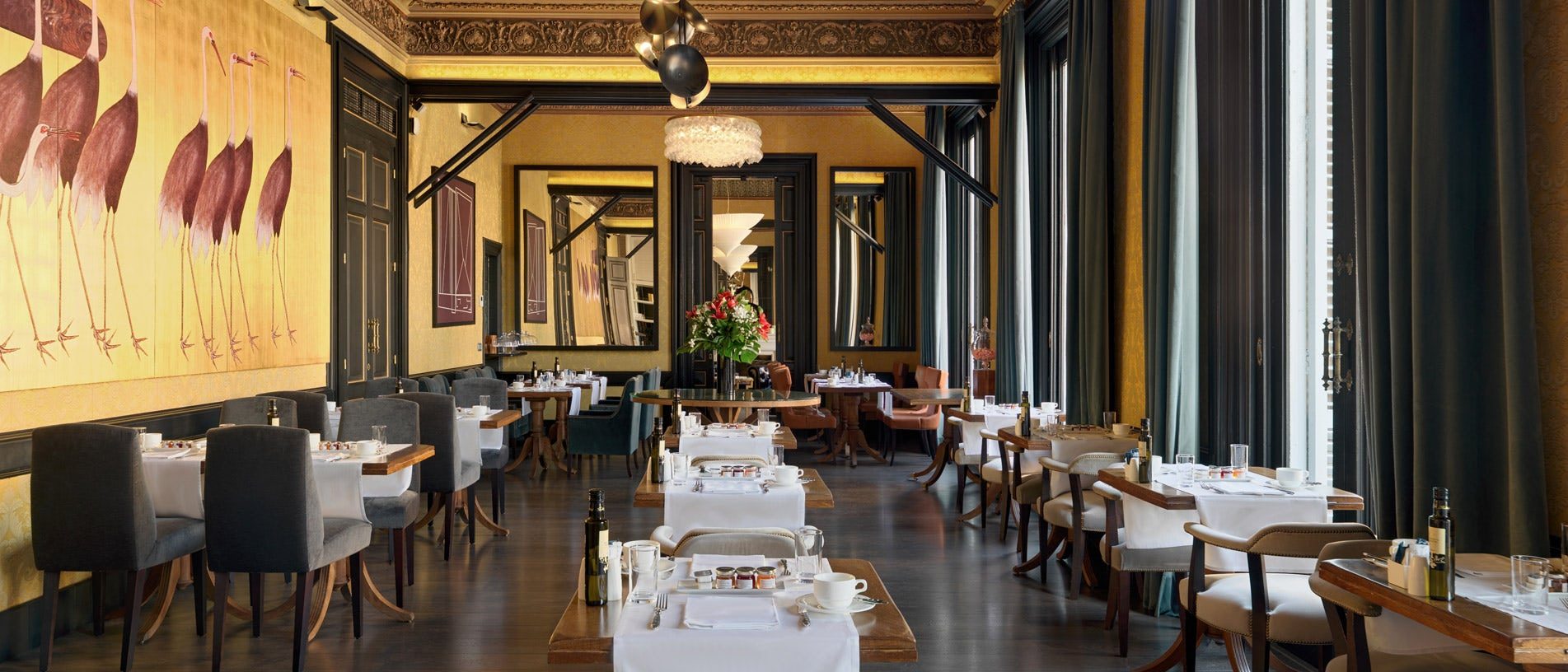 1892 Restaurant at H10 Catalunya Plaza with a gilded modernist ceiling, a flamingo mural, mirrored dining nooks, and tables set with white linen