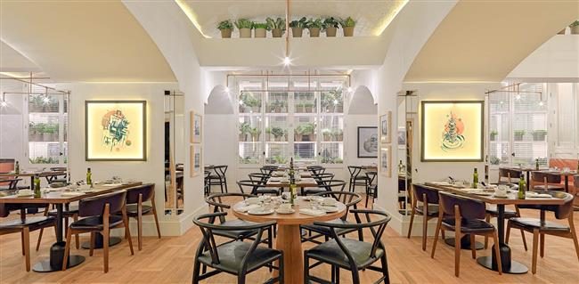 Market Restaurant at H10 Cubik with vaulted ceilings, hanging potted plants, framed artwork, and wishbone chairs around wood dining tables