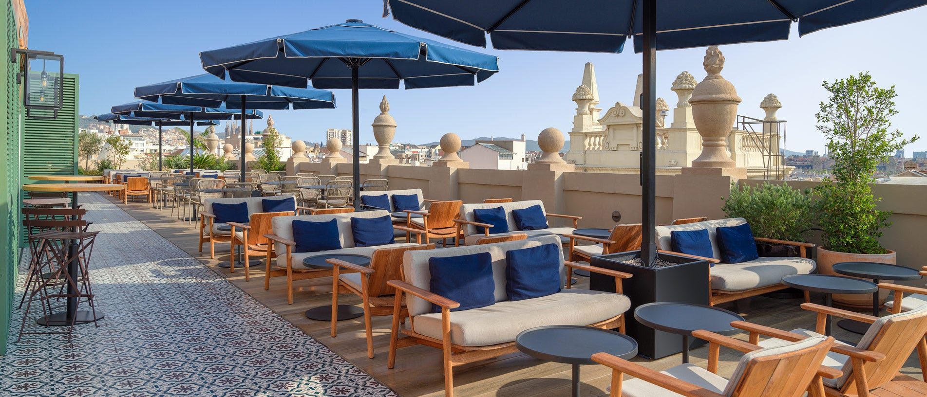 Rooftop terrace at H10 Madison with navy umbrellas over lounge seating and Gothic Quarter rooftops and spires in view