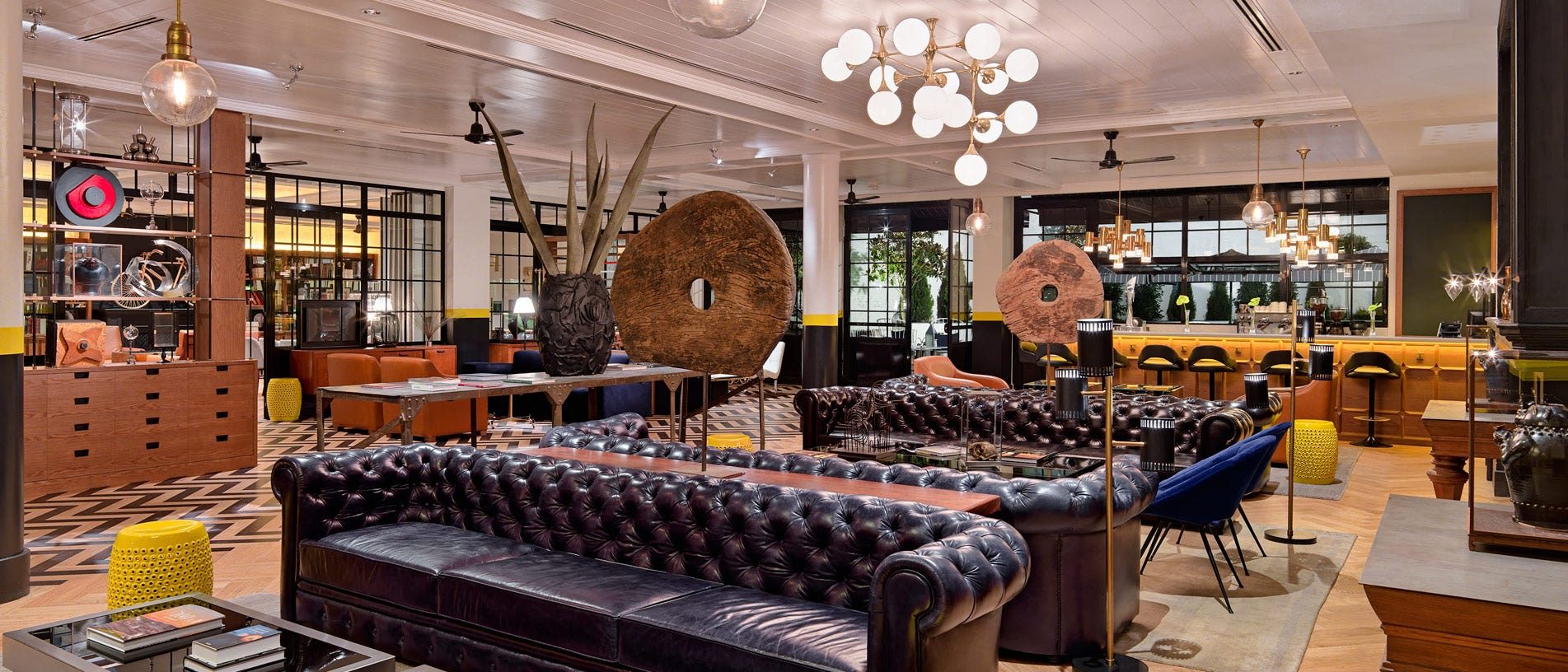 Eclectic lobby lounge at H10 Metropolitan with tufted black leather chesterfield sofas, a globe-bulb chandelier, and patterned tile floor