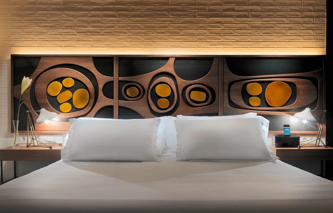 Classic double room at H10 Metropolitan with a white bed against a carved wood headboard featuring circular mid-century motifs