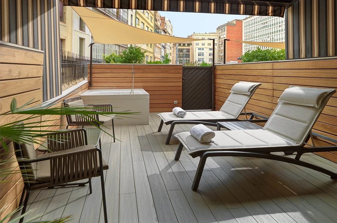 Private terrace of a Deluxe room at H10 Metropolitan with a built-in jacuzzi tub, wood slat walls, a sail-shade canopy, and lounge chairs