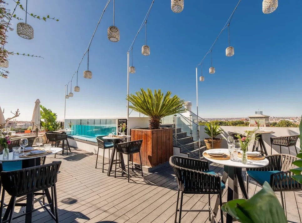 The glassed-in plunge pool on the rooftop terrace of El Cielo de Alcalá, with string lights, a palm tree and small dining tables around it.