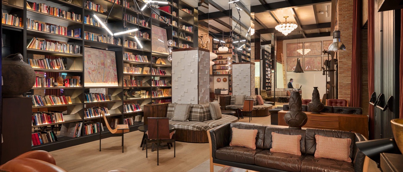 Hotel lobby lounge with floor-to-ceiling bookshelves, leather sofas and a patterned rug.