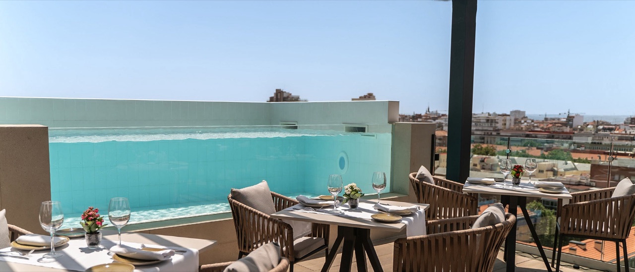 Rooftop terrace tables set for dining beside a glass-walled plunge pool with Madrid rooftops in the background.