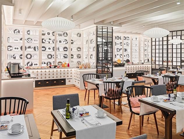 Urban Restaurant at H10 Universitat with a wall of illustrated ceramic plates, globe pendant lights, and mixed wood dining chairs