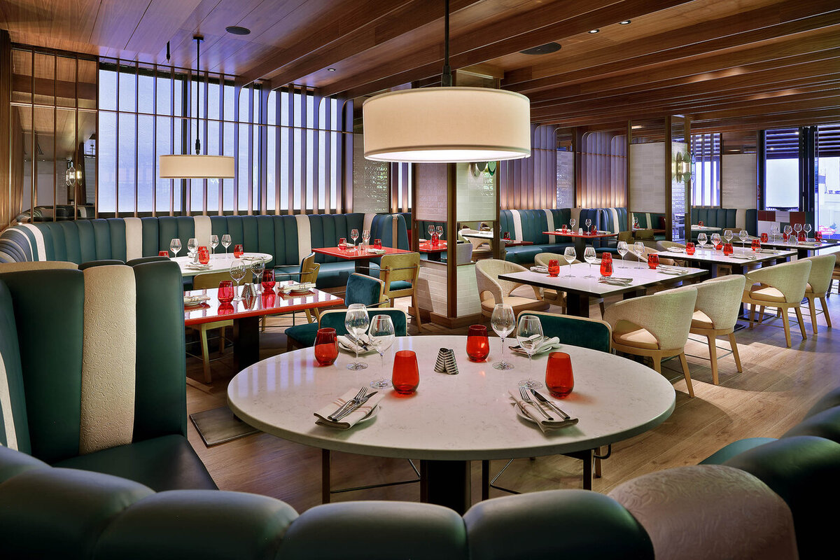 Empty Sessions Restaurant dining room with green banquette seating, round marble tables set with red glassware, and large windows.