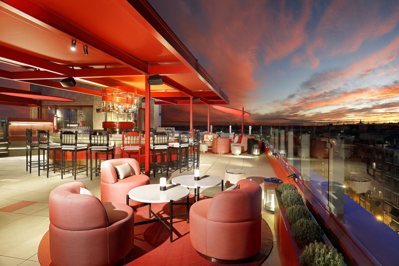 RT60 rooftop bar terrace at sunset, with a red illuminated canopy, bar stools and pink lounge seating overlooking the Madrid skyline.