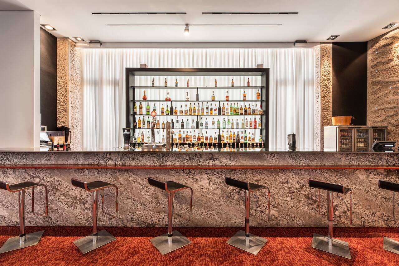 The Ferrum Bar counter with a backlit shelf of spirits bottles and a beer tap, empty bar stools in front.