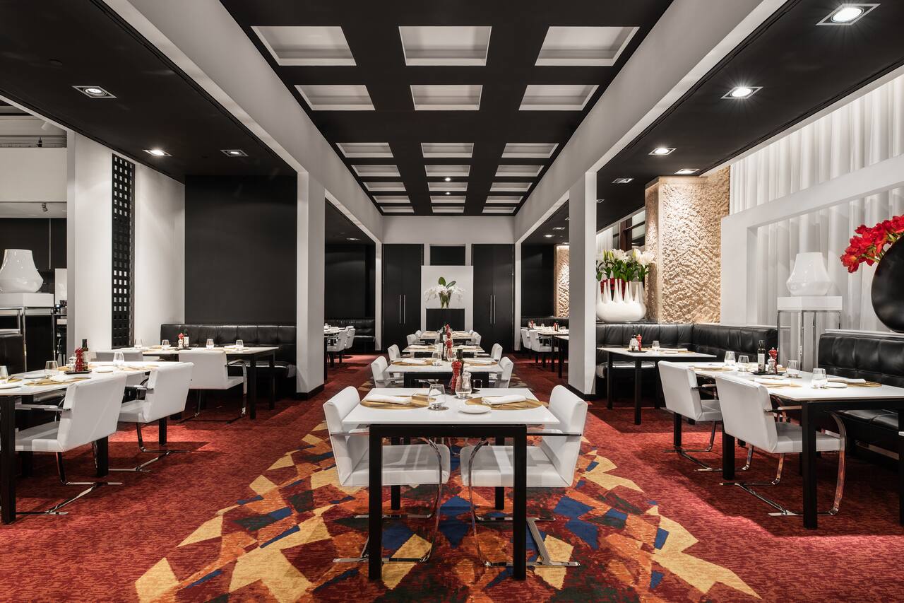 The Reserva Grill dining room, with white tables set for dinner under a black coffered ceiling and a red and gold patterned carpet.
