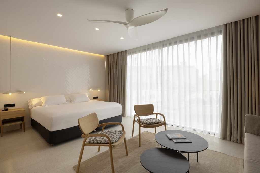 Double room at HM Palma Blanc with a herringbone-tiled headboard wall, pendant lights and two wooden armchairs around a coffee table.
