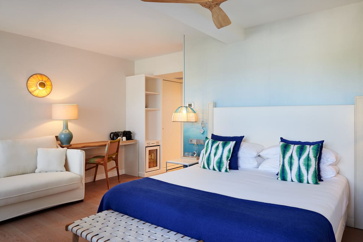 A colorful room at Hotel Honucai with a blue and white bed, a rattan pendant light and a small white sofa by the desk.