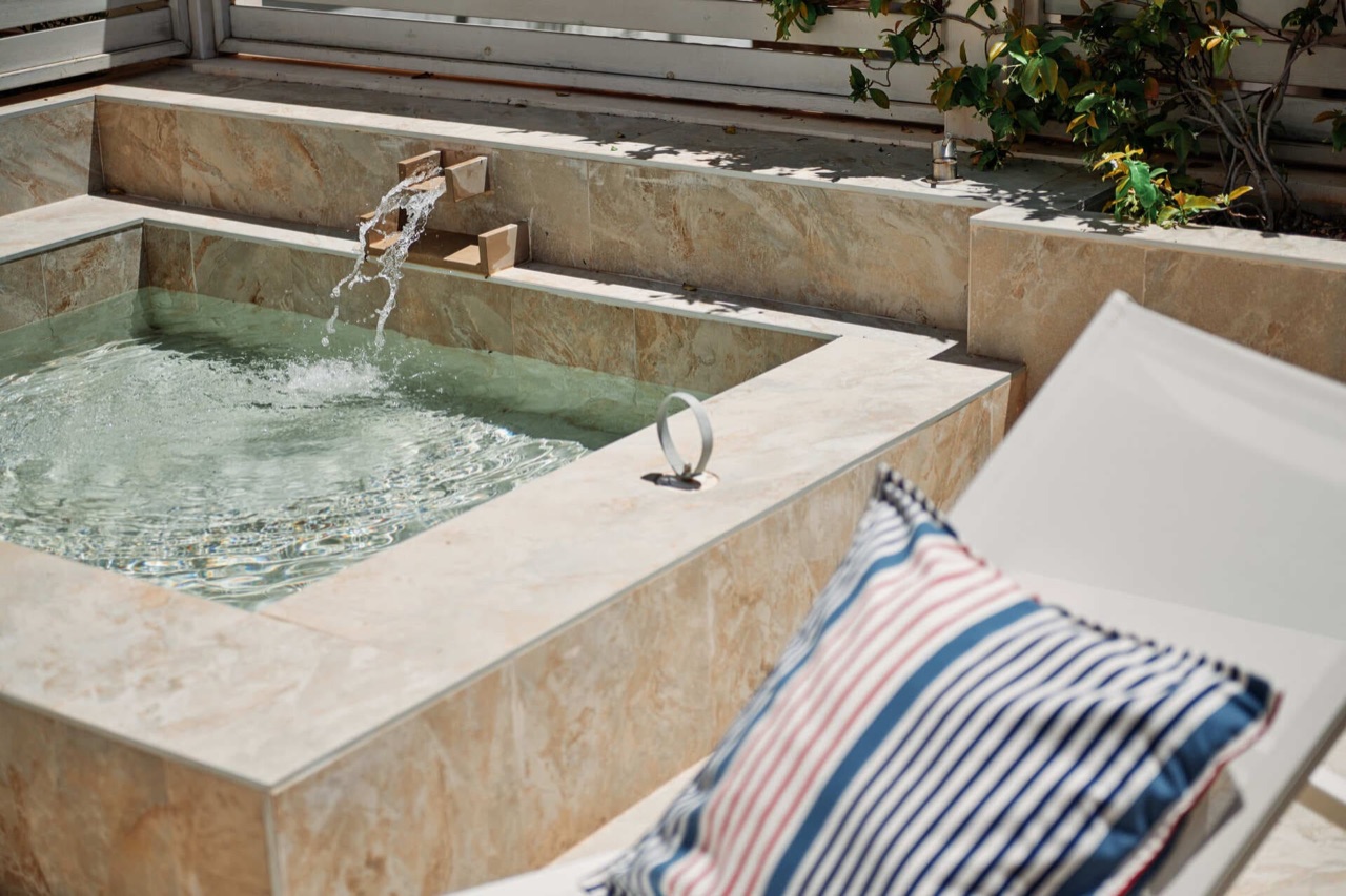 A small private plunge pool on a room terrace at Hotel Honucai, with a stone waterfall spout and a striped cushion on a lounger.
