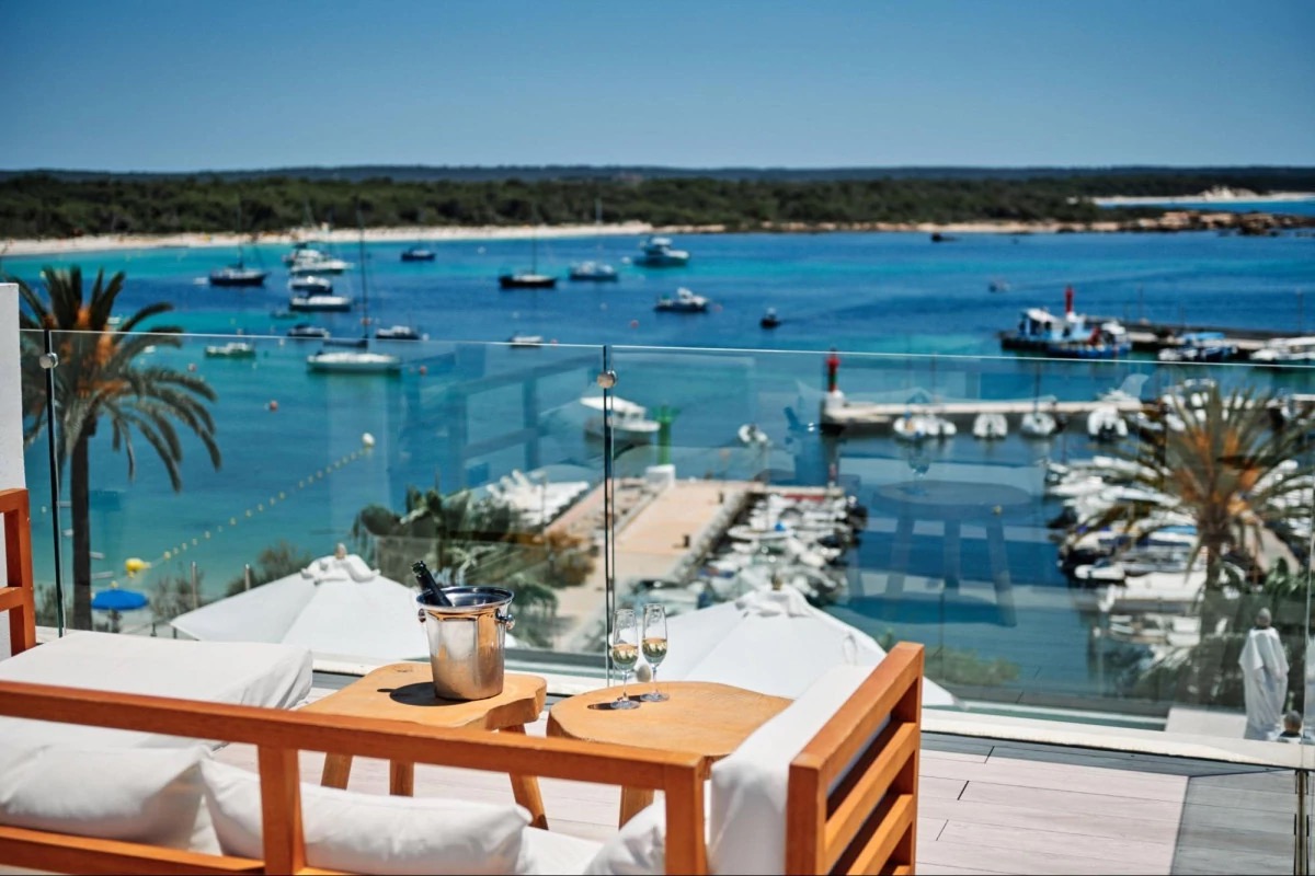 A rooftop terrace table at Hotel Honucai with a champagne bucket and two glasses, overlooking Colònia de Sant Jordi's marina and beach.