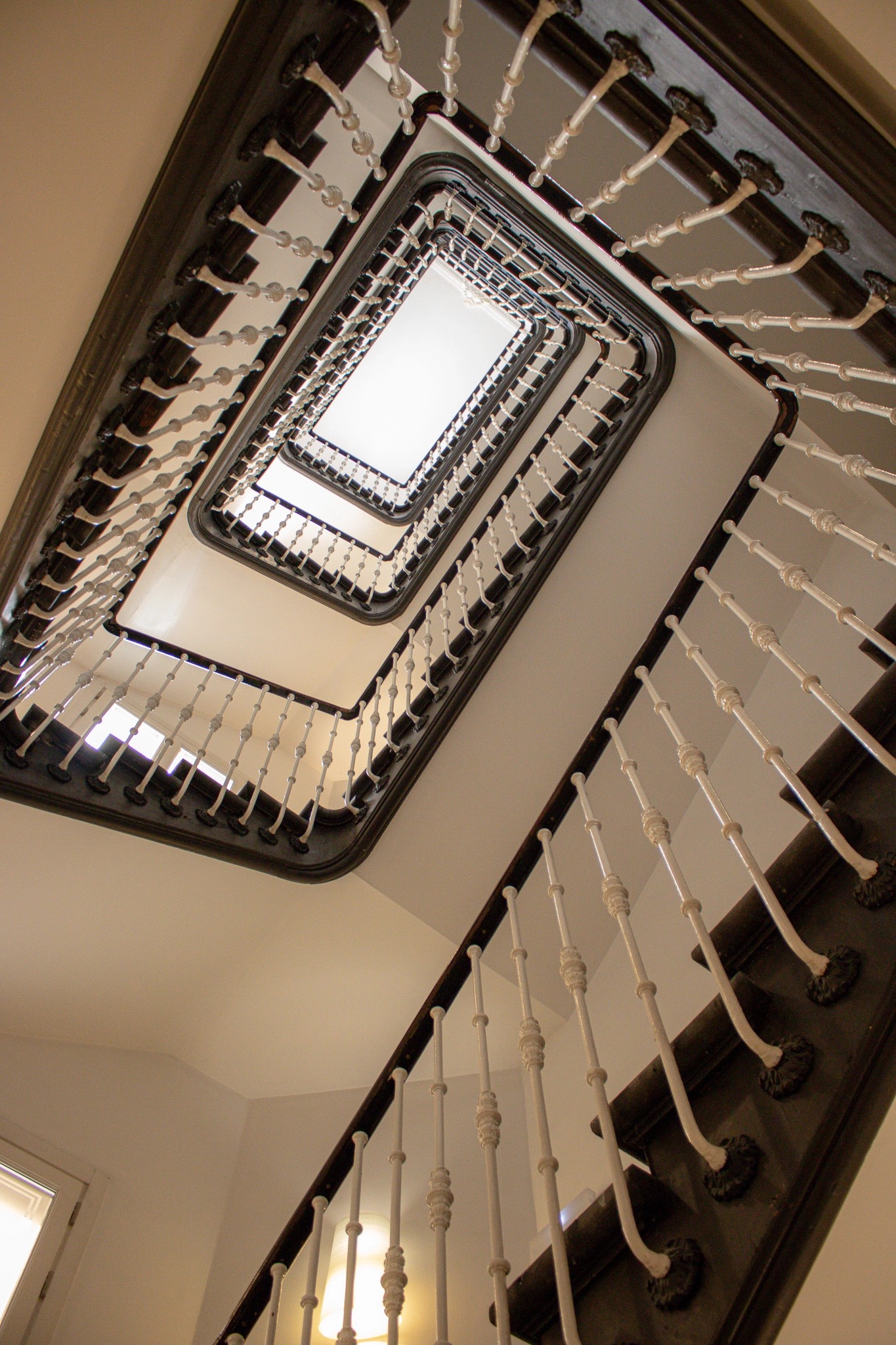 Looking up a multi-storey rectangular stairwell with dark timber handrails, white cast-iron balusters and a skylight at the top.