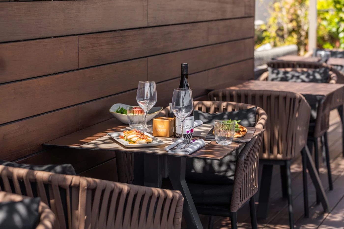 Terrace table at La Isabela restaurant, Hotel 1898, set with wine glasses and small plates against a wood-slat wall in dappled sunlight