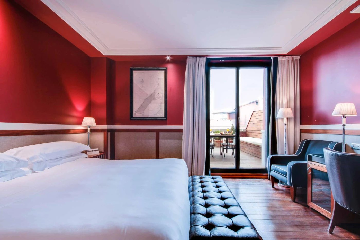 Deluxe room at Hotel 1898 with deep red walls, a tufted black bench at the foot of the bed, and glass doors opening onto a private terrace