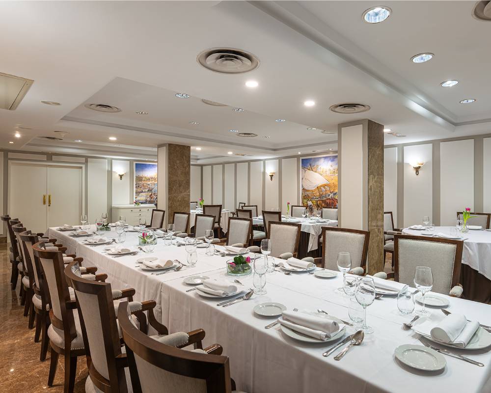 A banquet-style dining room at Las Arenas restaurant, with long tables set for a group meal under mural-covered walls.